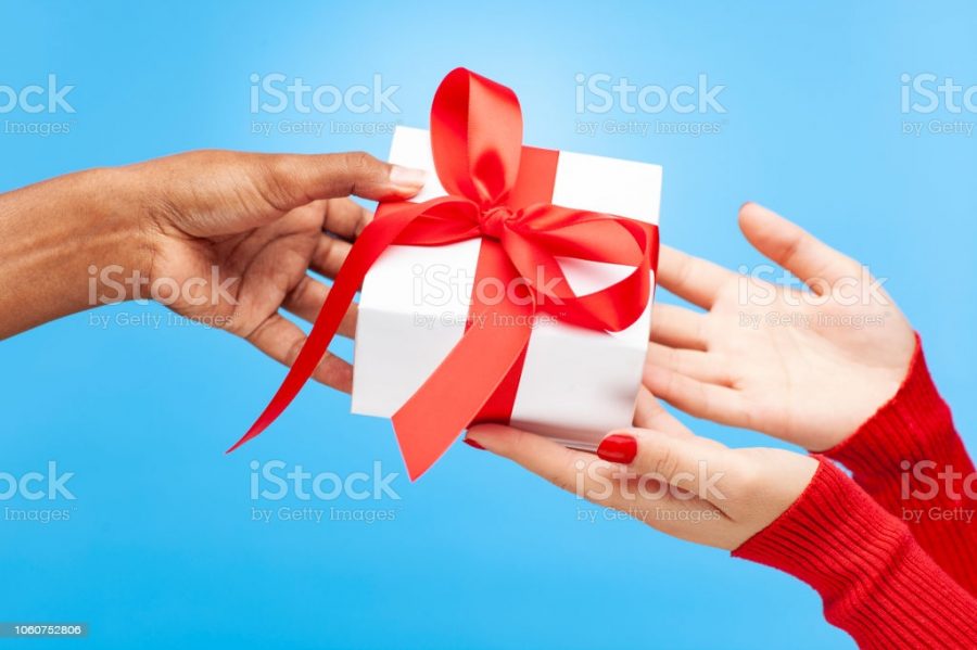 Close up womens hands giving and receiving a white gift box tied with a red bow. Isolated on a blue background image.