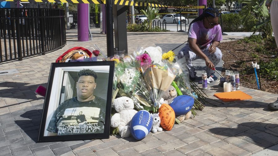 Visitors stand next to a memorial while a family member lights candles for Tyre Sampson, 14, who was killed when he fell from the Orlando Free Fall ride at ICON Park in Orlando, Florida, on March 26, 2022. (Willie J. Allen Jr./Orlando Sentinel/Tribune News Service via Getty Images)